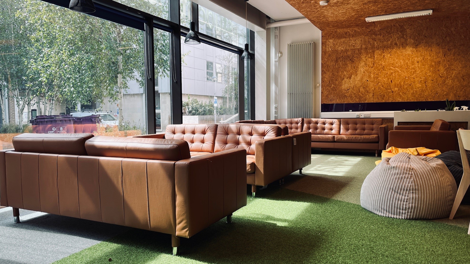 Brown leather-feel sofas are arranged in The Hive, next to a big window overlooking green space